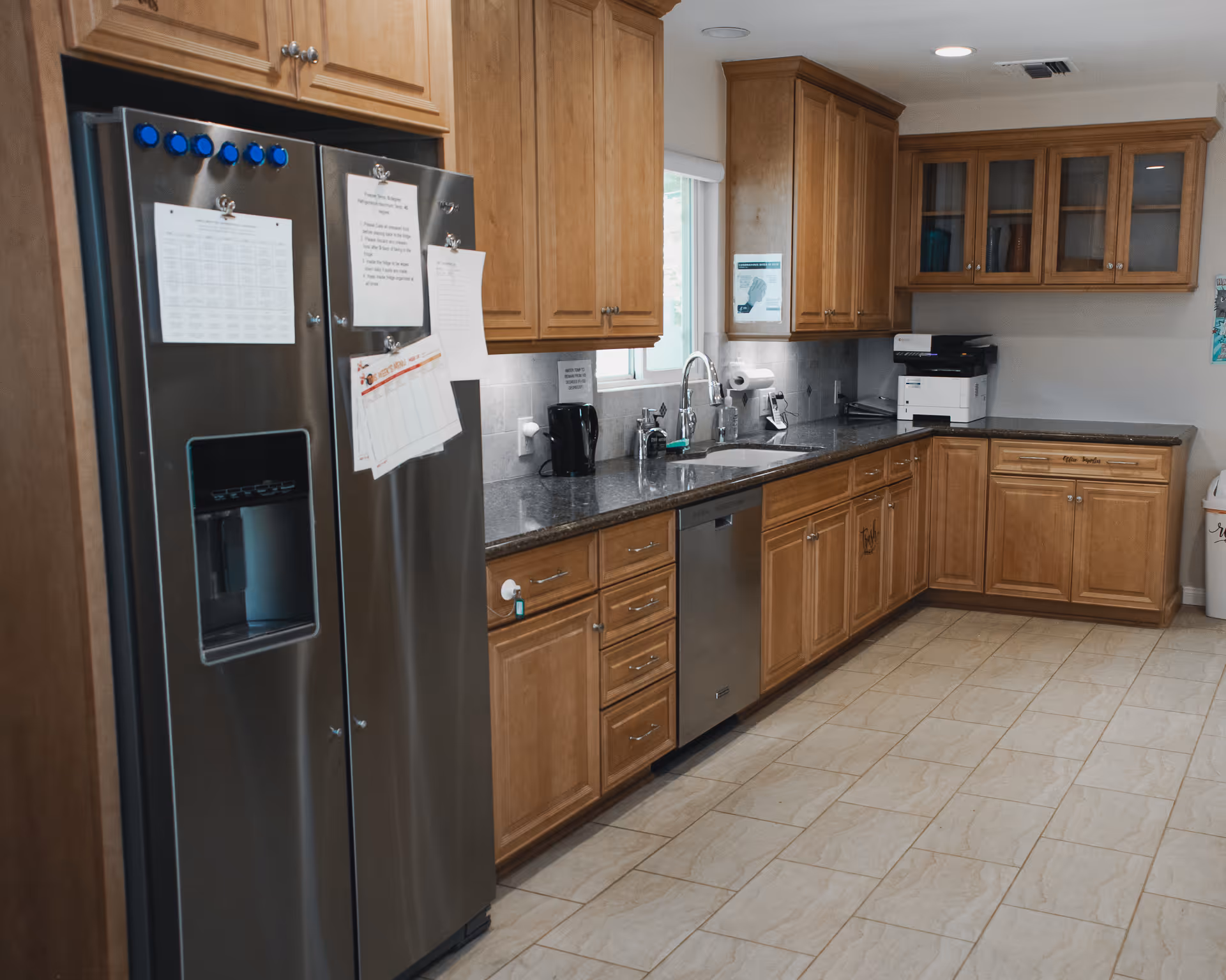 A spacious kitchen with wooden cabinets, stainless steel refrigerator, dishwasher, sink and granite countertops.