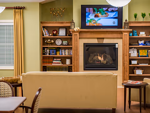 Community living room with a sofa facing a fireplace and wall-mounted TV flanked by bookshelves.