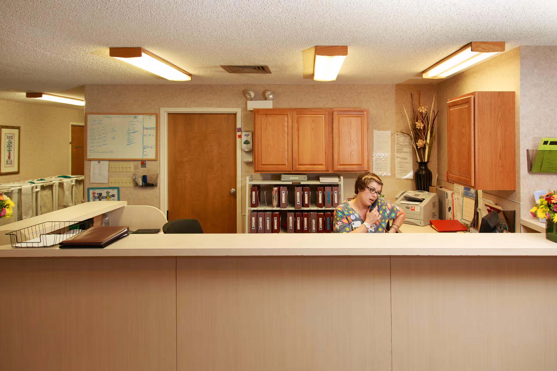 Reception desk inside a senior living facility with a staff member talking on the phone behind the counter.