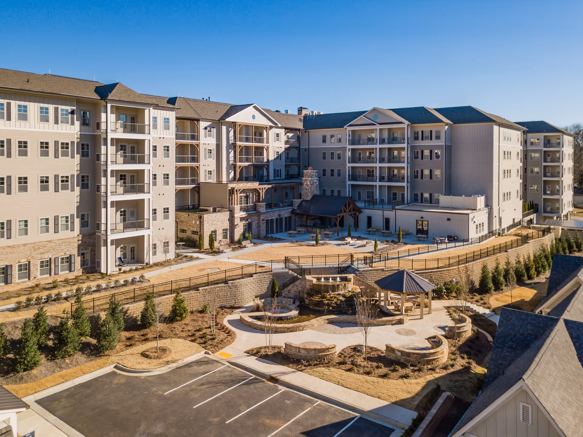 Aerial view of a multi-story senior living building with balconies surrounding a landscaped courtyard featuring a fountain and gazebo.