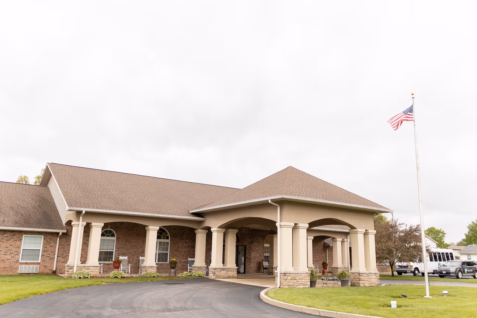 Exterior view of Cedar Trails Senior Living facility showing a single-story building with a covered entrance supported by columns, a paved driveway, green lawn, and an American flag on a flagpole.