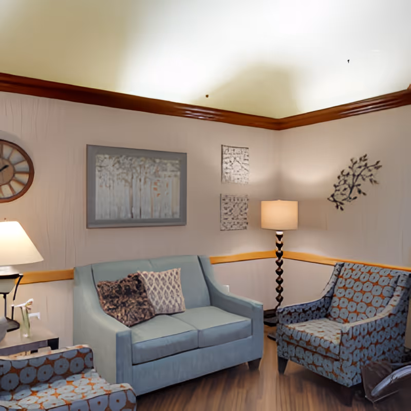 Cozy seating area with a sofa, two patterned armchairs, floor and table lamps, and framed wall art.