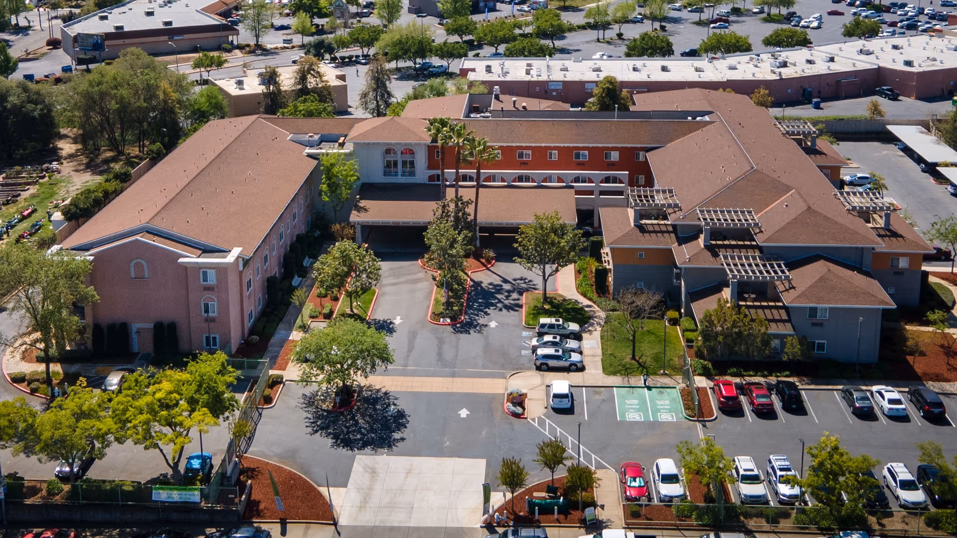 Aerial view of a multi-wing senior living facility with a central driveway, parking lot, and landscaped grounds.