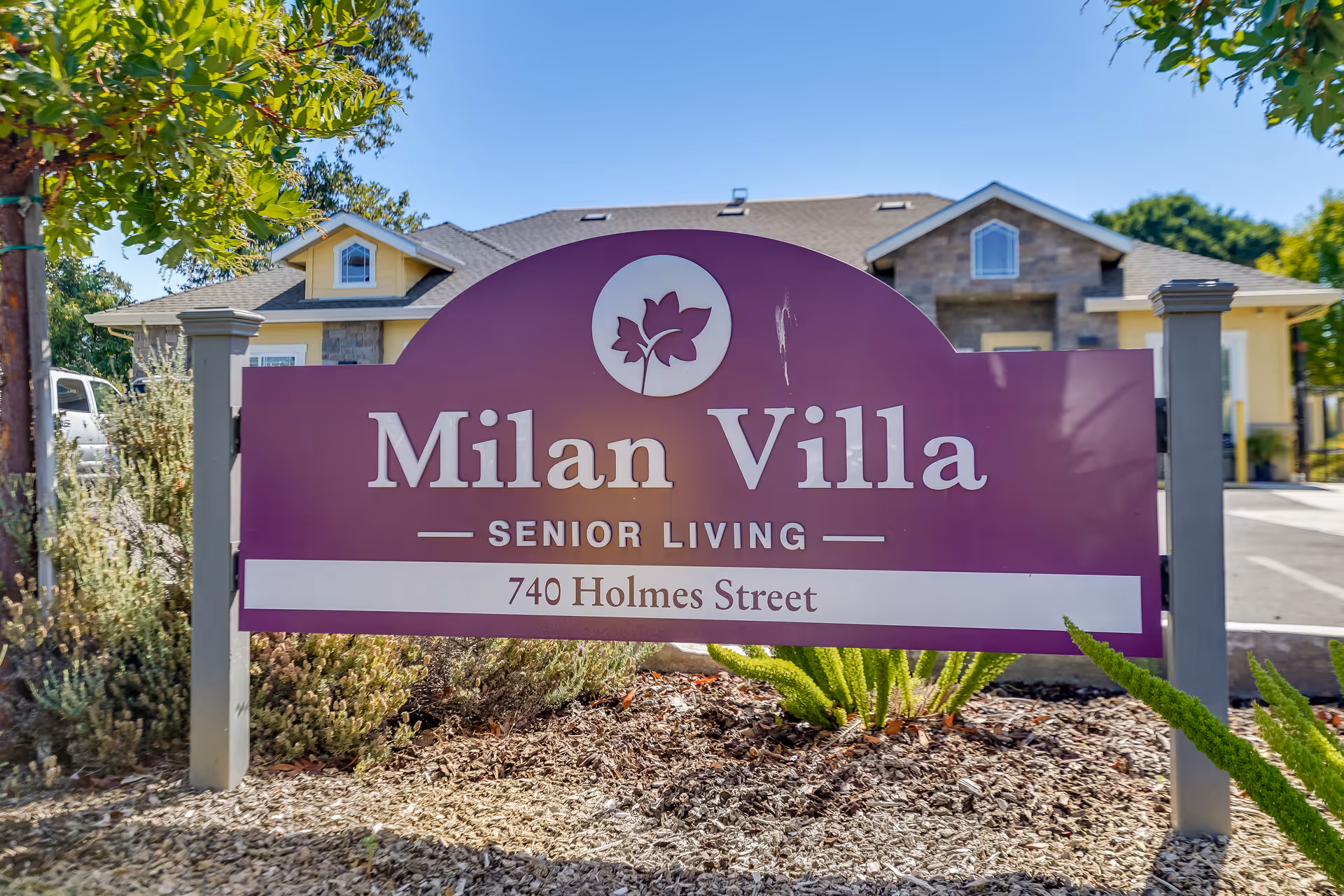 Purple sign reading "Milan Villa Senior Living, 740 Holmes Street" in front of a residential building