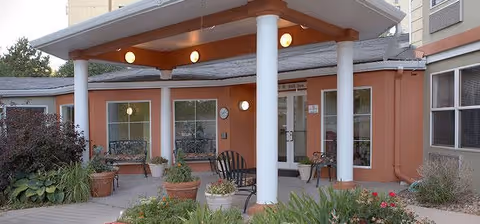Entrance area of Dayspring Villa featuring a covered porch with white columns, outdoor seating including benches and chairs, potted plants, and surrounding greenery.
