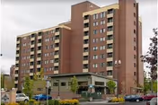 Multi-story brick residential building with a landscaped front entrance and parked cars along the street.