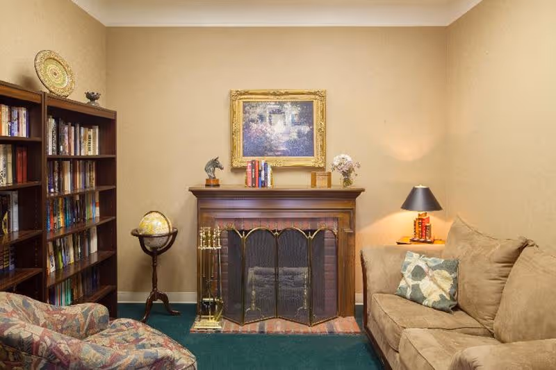 Cozy living room with a central fireplace flanked by bookshelves, a globe, a sofa and an armchair beneath a framed painting.