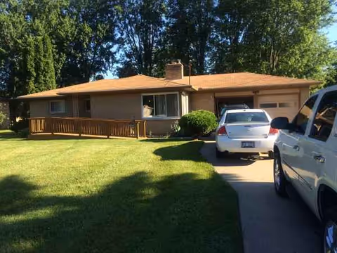 Exterior view of Granny's Place: a single-story beige house with a driveway and parked cars.