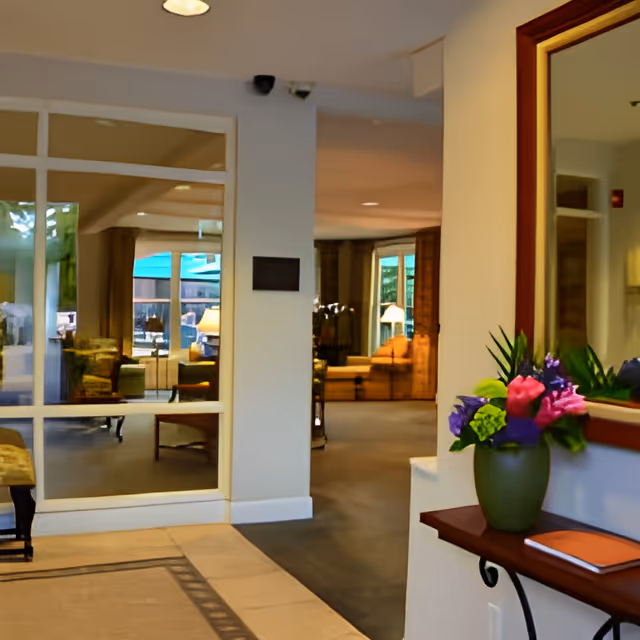 Lobby/common area with seating visible through glass panels and a console table with a vase of flowers in the foreground.