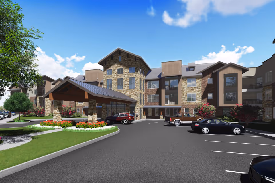 Exterior view of a senior living facility named Watermere at the Preserve, showing a multi-story building with stone and wood siding, a covered entrance, parked cars, landscaped greenery, and a bright blue sky with some clouds.