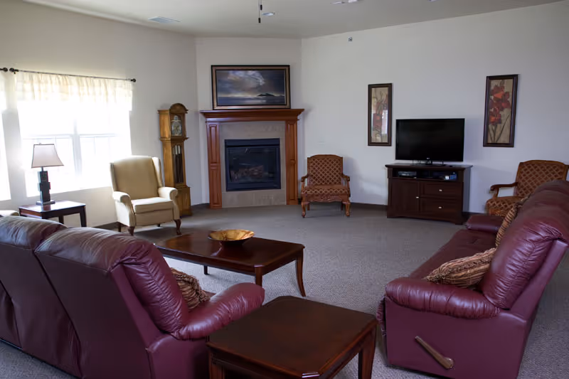 Spacious common living room with burgundy leather sofas, armchairs, a fireplace, coffee table, and a TV.