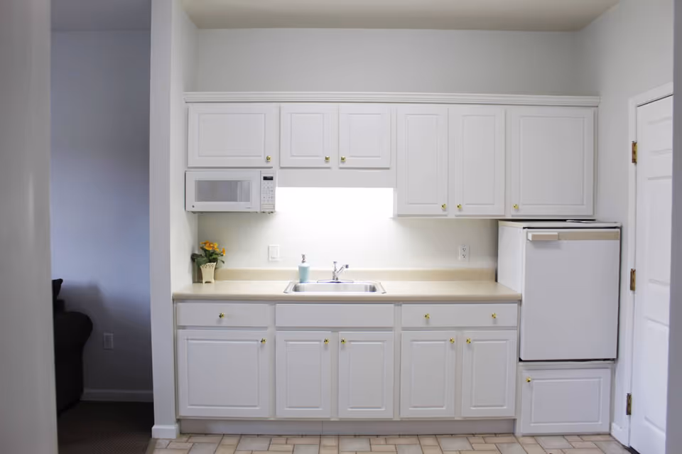 Small kitchenette with white cabinets, a sink, microwave, and compact refrigerator.