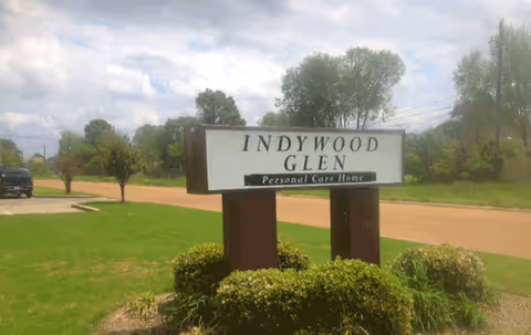 Outdoor sign for Indywood Glen Personal Care Home on a grassy lawn with shrubs.