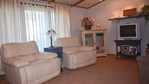 Two cream recliners sit in a cozy living room with a TV.