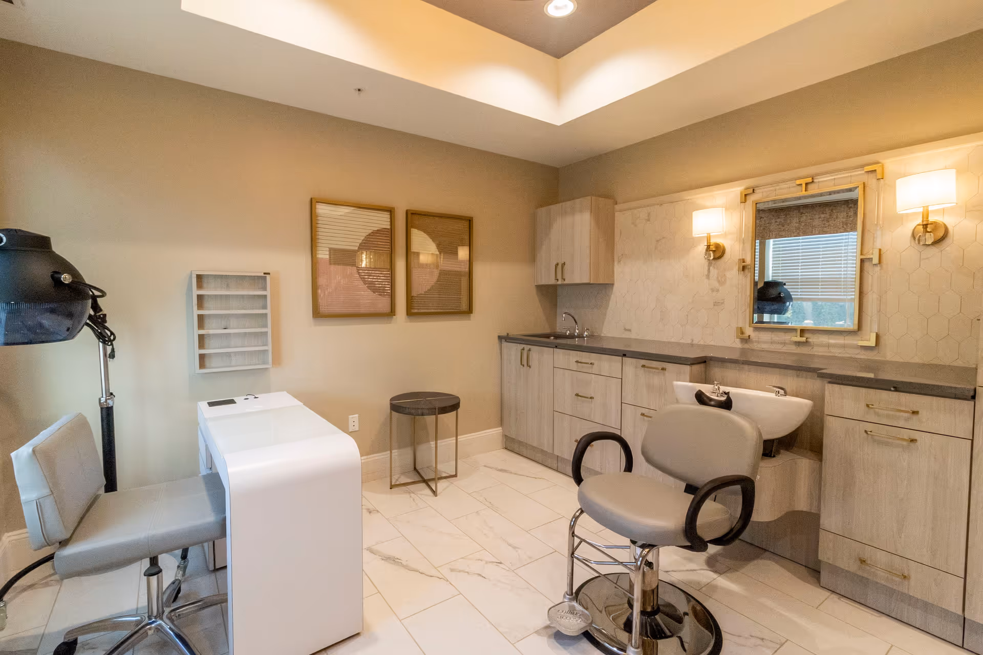 A bright salon-style room with a styling chair by a shampoo sink, manicure table, cabinets, and a mirror.