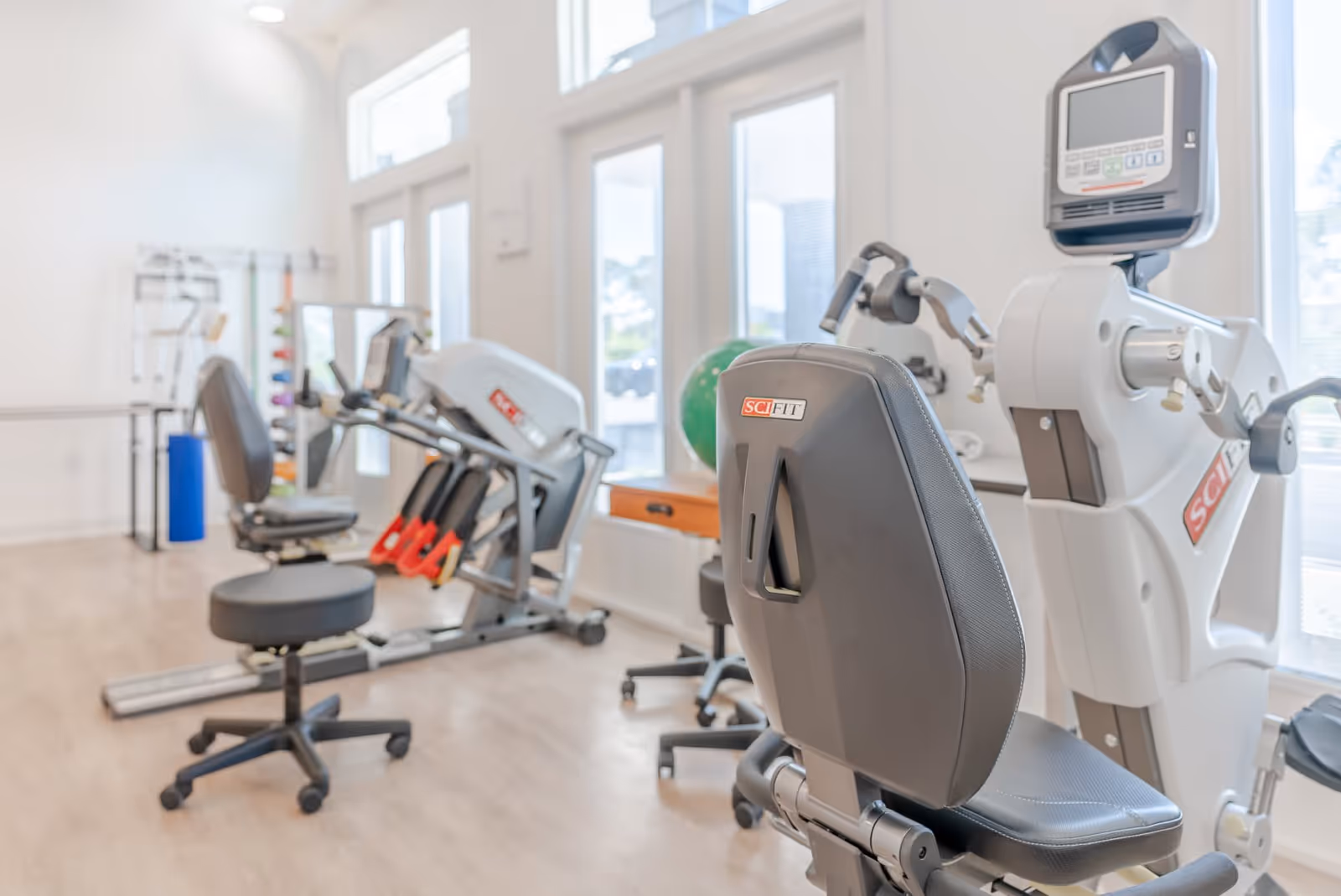 Bright exercise/therapy room with seated cardio and strength machines and large windows.