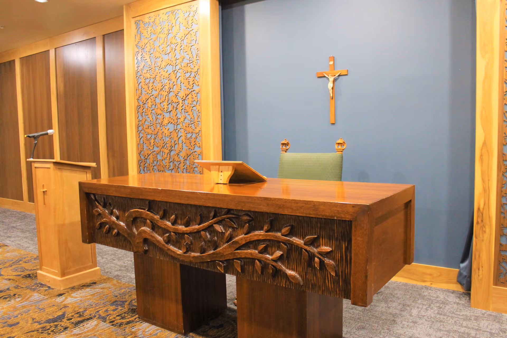Wooden altar and lectern in a small chapel with a crucifix on a blue wall behind them.
