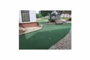 Small outdoor putting green with benches and landscaped gravel paths next to a brick building.