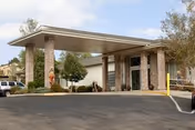 Covered drive-up entrance with brick columns and glass doors at the front of a single-story building with landscaping and a paved driveway.