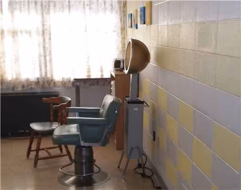 Barber chair and styling station in a pastel-tiled interior of a senior facility.