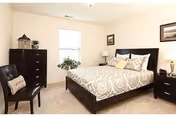 Furnished bedroom with a patterned bedspread on a dark wood bed, matching nightstands and dresser, a chair, and a window.