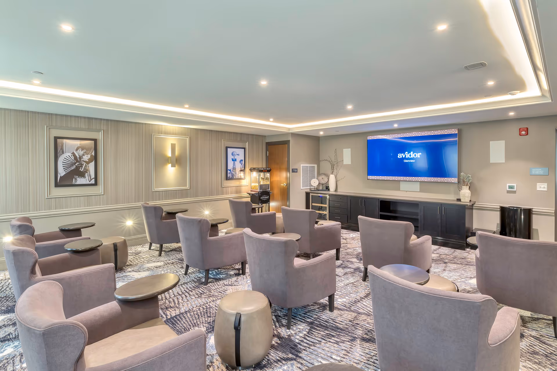 A comfortable media lounge with multiple upholstered armchairs and small tables facing a large wall-mounted TV.
