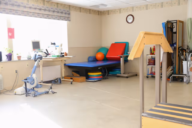 Bright therapy/exercise room with a treatment table, exercise bike, balance equipment, and therapy balls.