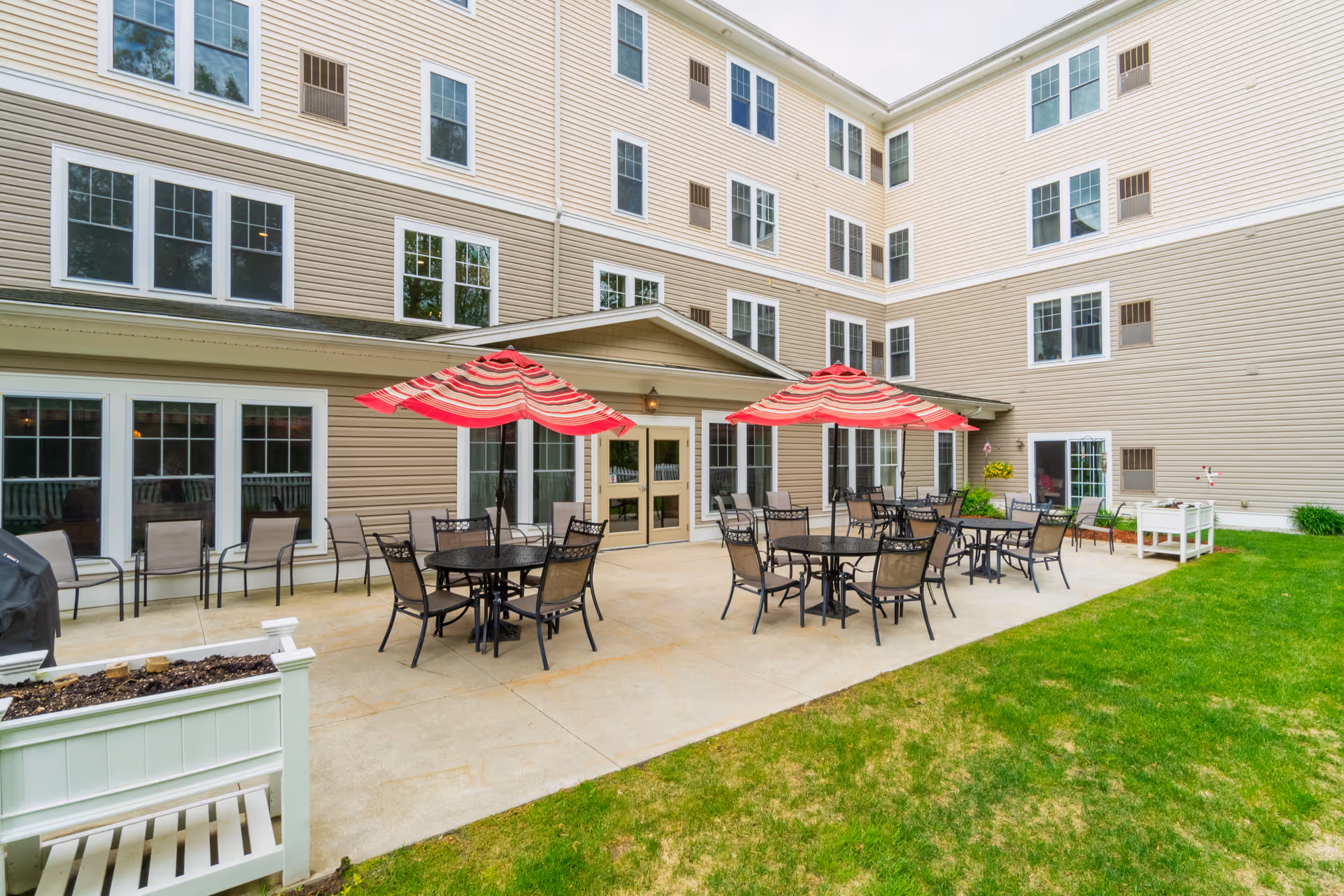 Outdoor patio with round tables and chairs under red-striped umbrellas in front of a multi-story beige building.