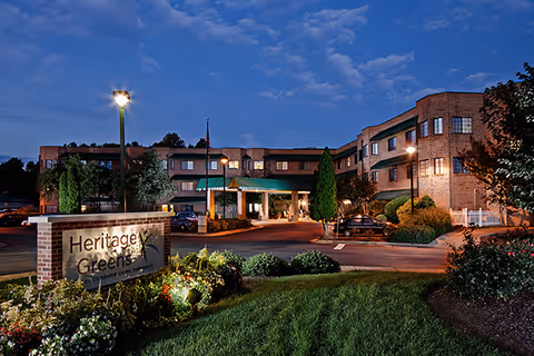 Evening exterior view of Heritage Greens senior living facility with illuminated entrance.