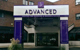 Front entrance canopy with purple signage reading 'ADVANCED Center for Nursing & Rehabilitation' on a brick building.