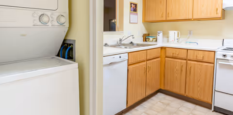 Small apartment-style kitchen with oak cabinets, white appliances, and a stacked washer-dryer unit visible in the doorway.