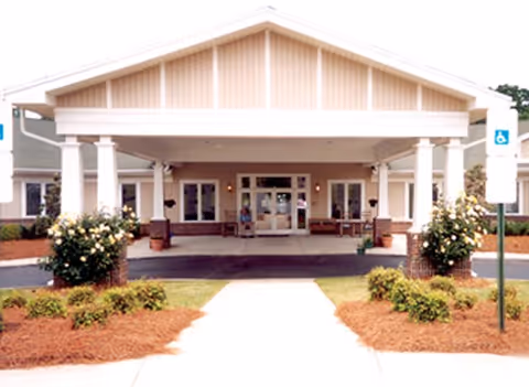 Front entrance of the Woodridge senior living facility with a covered portico, columns, and a landscaped walkway.