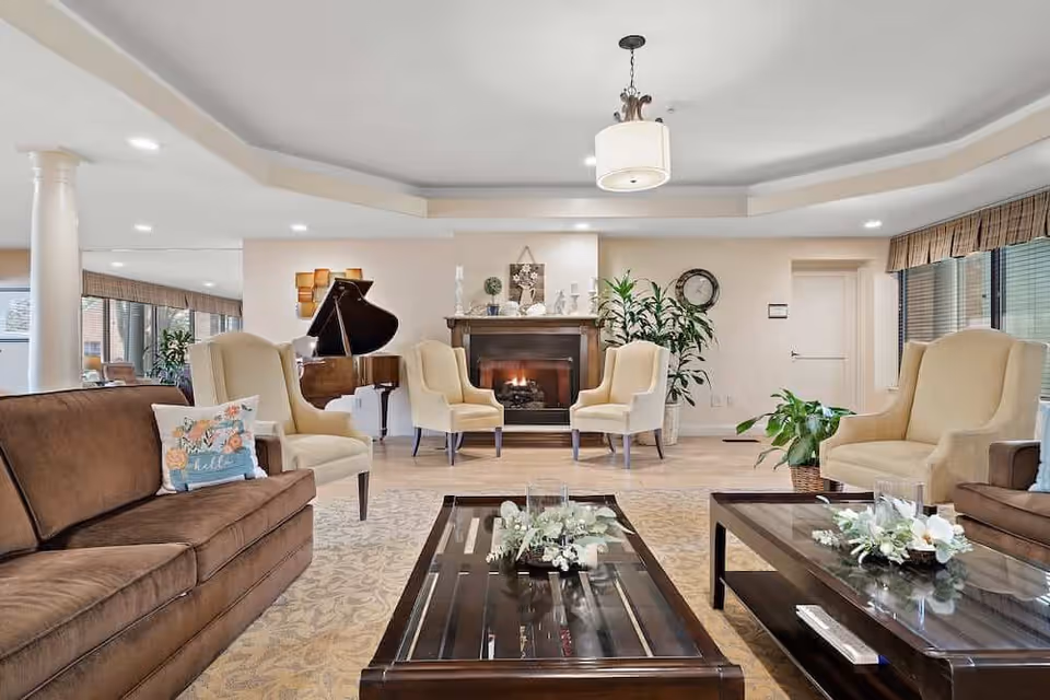 Spacious lounge with sofas and armchairs arranged around coffee tables facing a fireplace and a grand piano in the background.