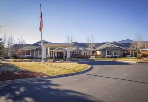 Sunrise of Boulder facility exterior with driveway, flagpole, and entrance under clear sky.