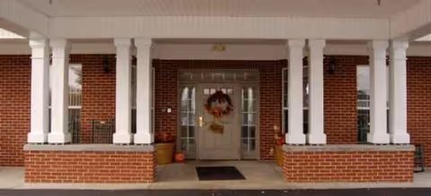 A brick building front with white columns, double doors, wreath, and planters at entrance.