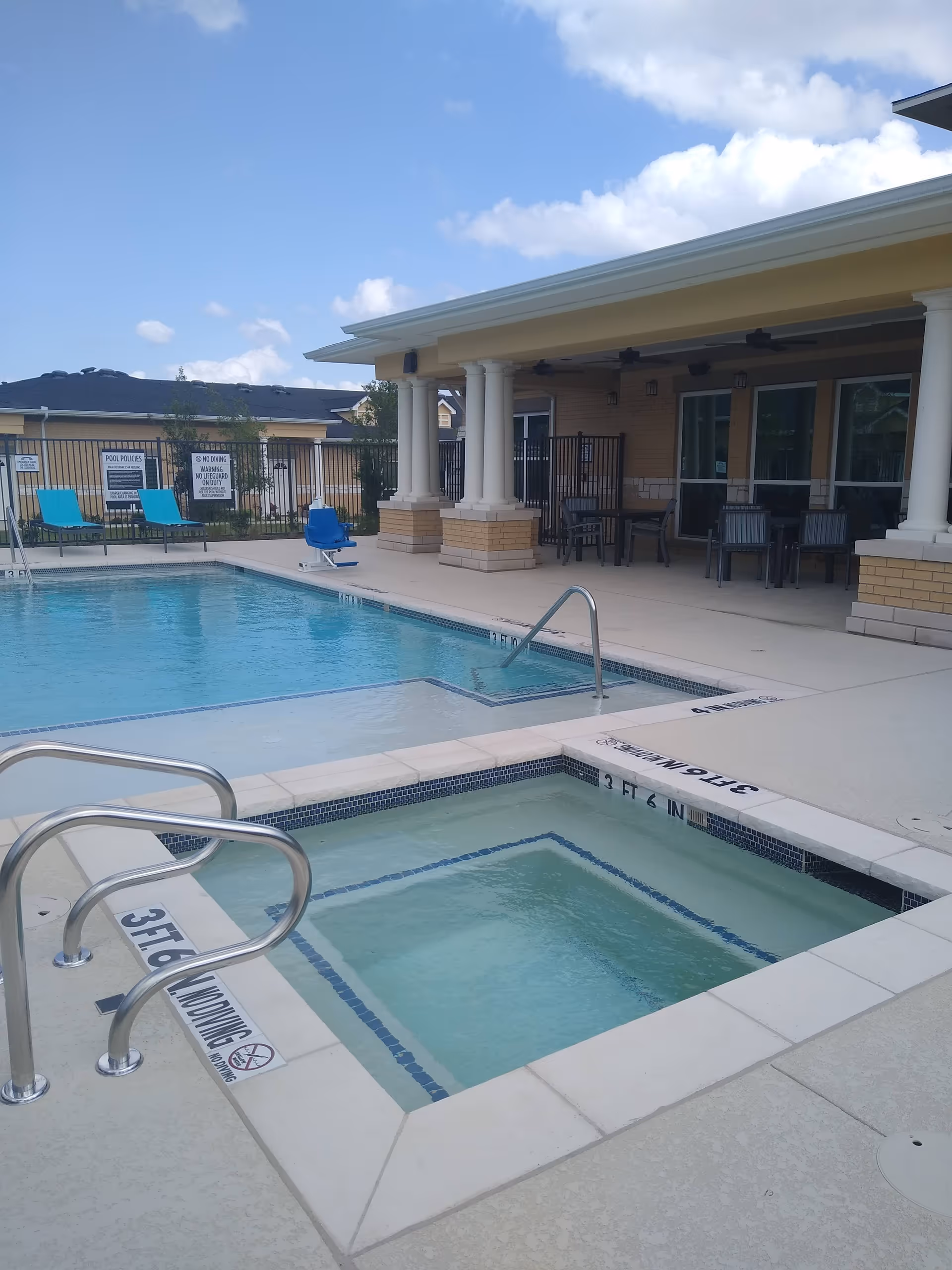 Outdoor swimming pool and adjacent hot tub with lounge chairs and a covered patio supported by columns.