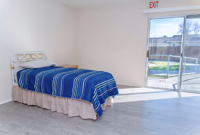 A single bed with blue striped bedding sits in a bare bedroom near a sliding door.