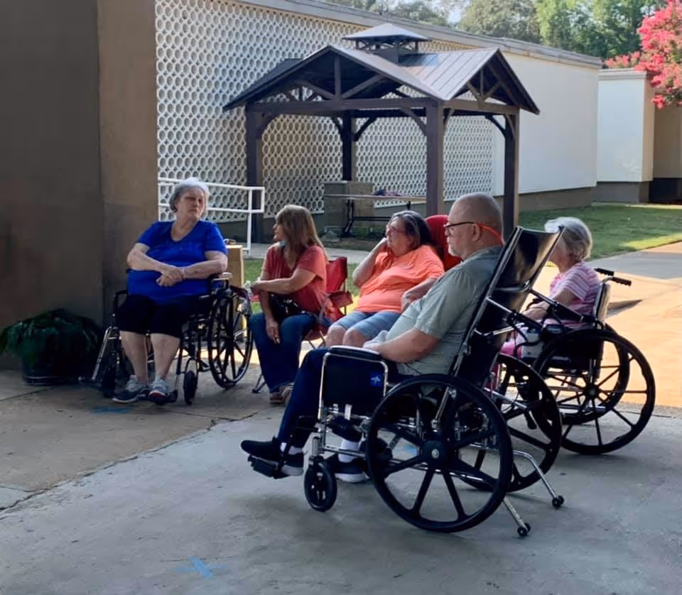 Group of people in wheelchairs sitting outside in a courtyard.