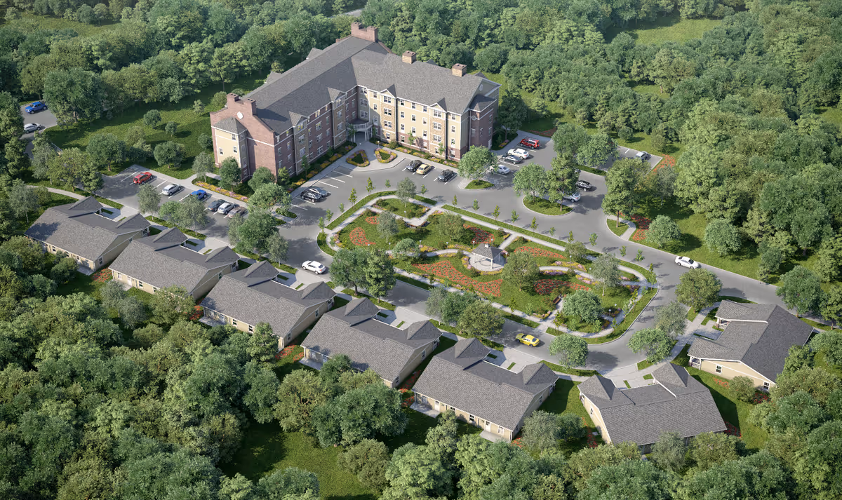 Aerial view of Riverside Landing at Delaware Place senior living facility showing multiple buildings surrounded by dense trees. The main building is a large multi-story structure with parking spaces around it. Several smaller single-story buildings are arranged in a semi-circle around a landscaped garden area with walking paths and benches.