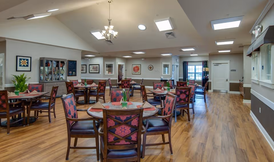 Spacious dining room with multiple round tables and patterned chairs on wood flooring under skylights and chandeliers.