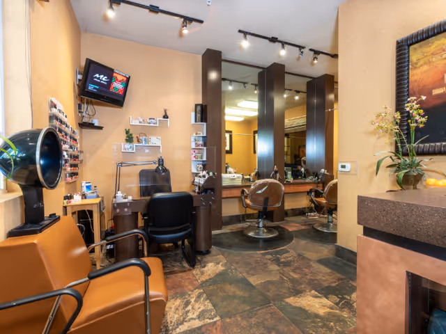 Interior view of a salon area within a senior living facility featuring salon chairs, mirrors, a hair dryer, nail polish display, and a small television mounted on the wall.
