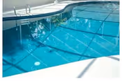 Clear blue swimming pool with a metal ladder and surrounding deck under a screened enclosure.