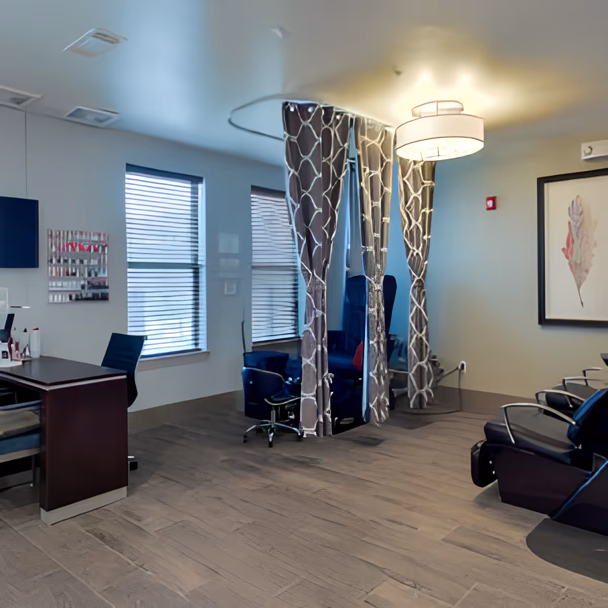 Interior salon-style common room with seating, curtained pedicure stations, a desk and large windows.