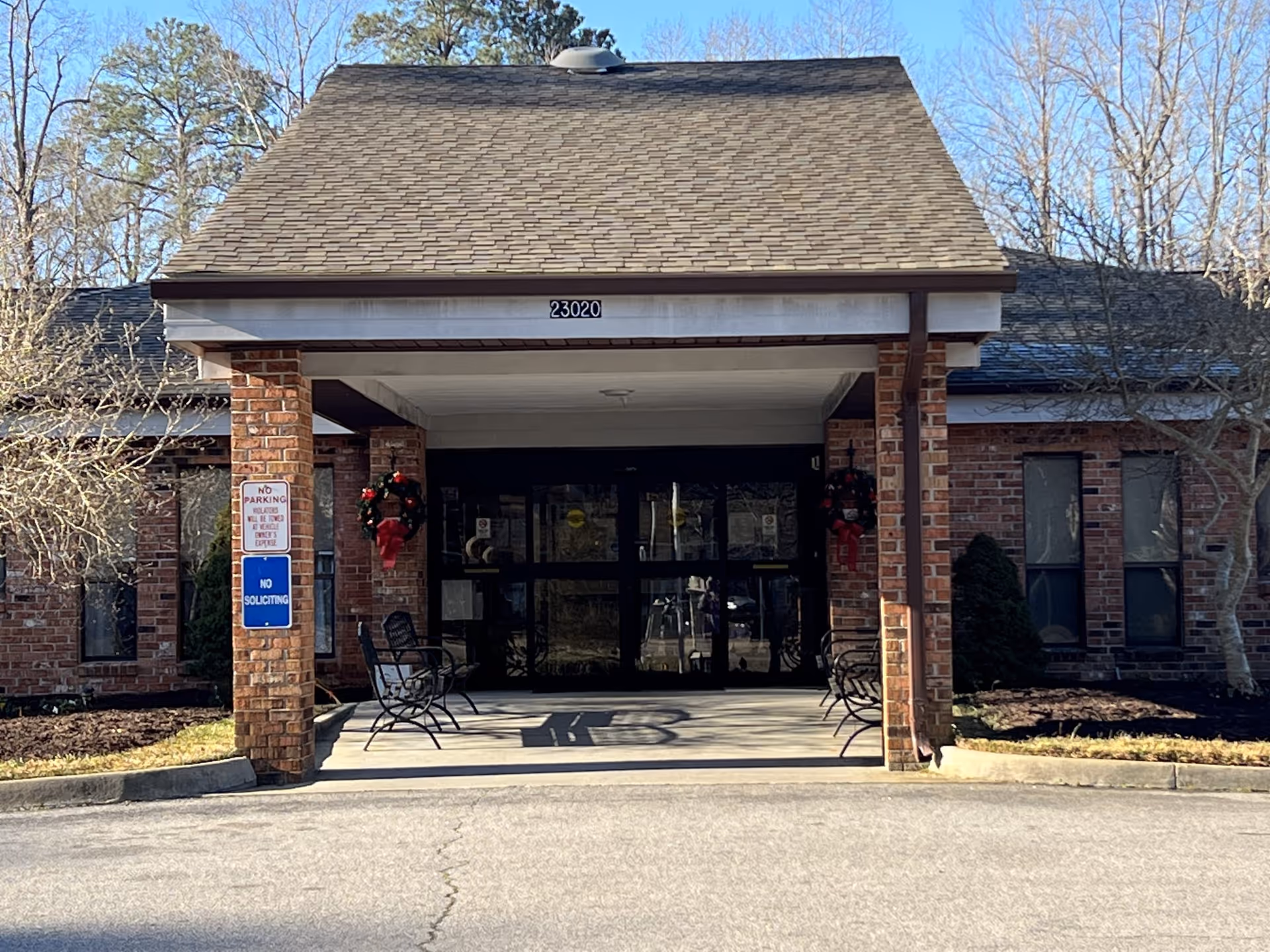 Entrance to a brick senior living center with a covered drop-off and chairs.