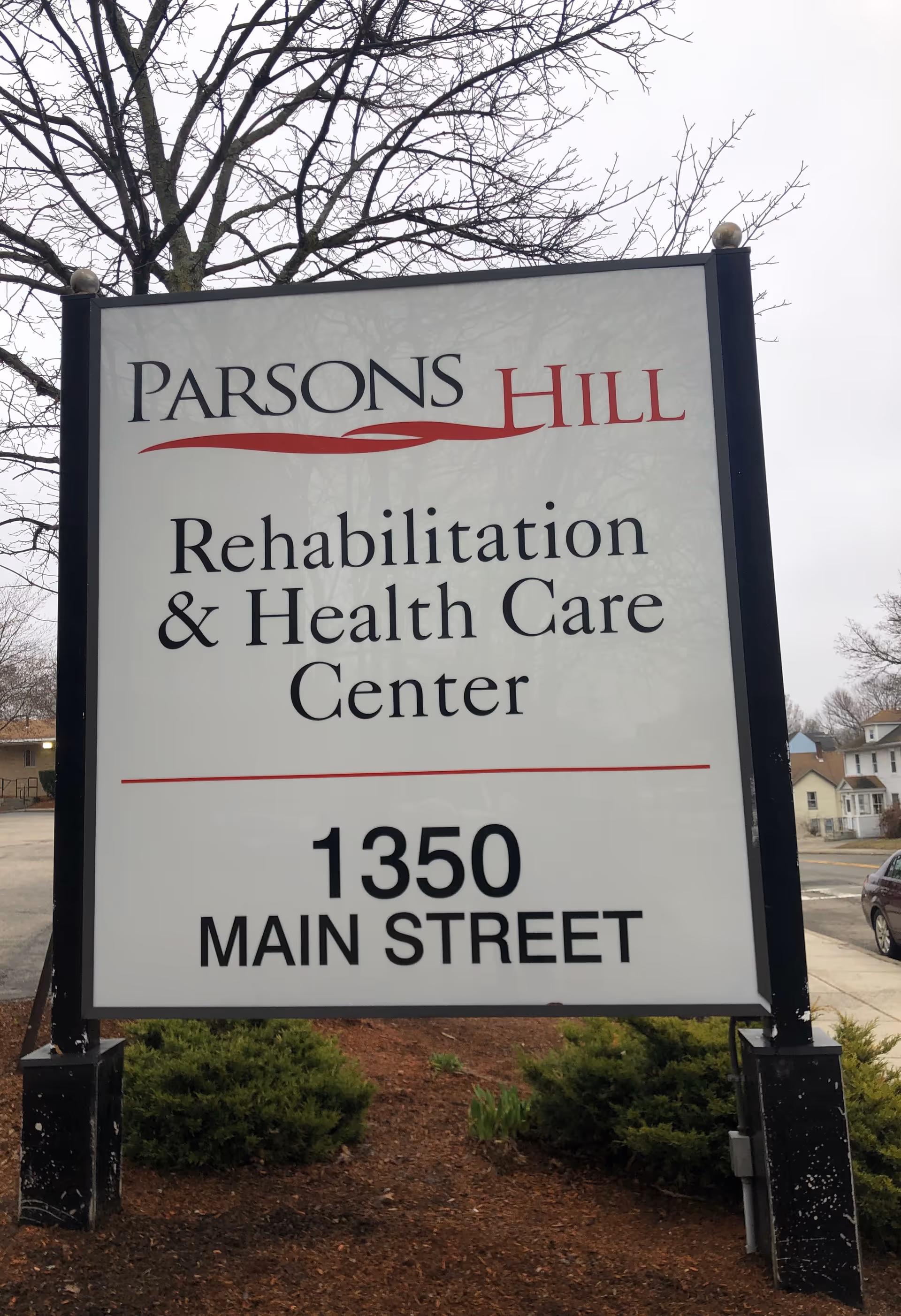 Outdoor sign for Parsons Hill Rehabilitation & Health Care Center located at 1350 Main Street, with trees and houses in the background.