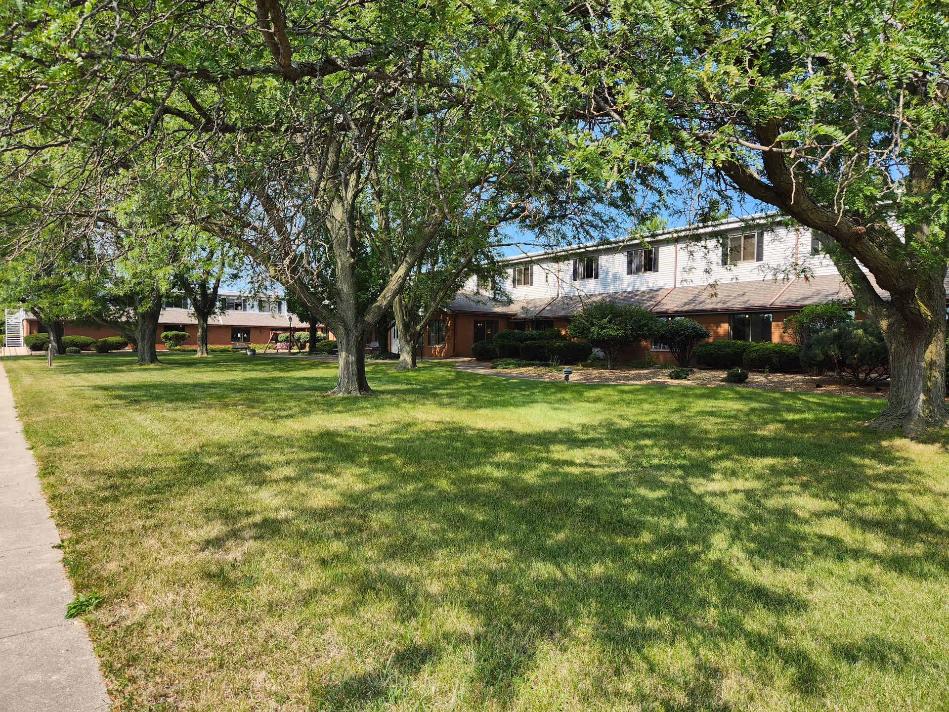 Two-story brick and siding retirement building with a wide grassy lawn and mature trees in front.