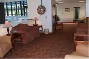 Carpeted lobby seating area with sofas, side tables and lamps leading toward a hallway and entrance.