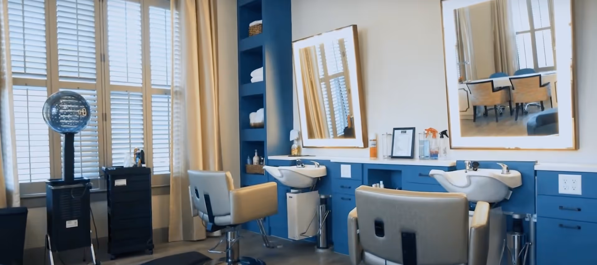 Interior salon area with two hair-washing stations, styling chairs, mirrors, shelving and large shuttered windows.