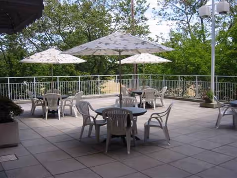 An outdoor terrace with round tables, chairs, and large umbrellas amid greenery.
