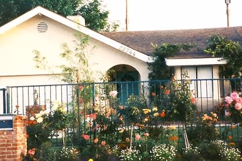 Clarendon Senior Living front exterior with arched entry and colorful rose garden behind a metal fence
